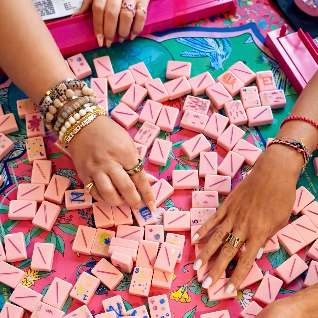 Hands arranging colorful wooden blocks on a game board with pink borders.