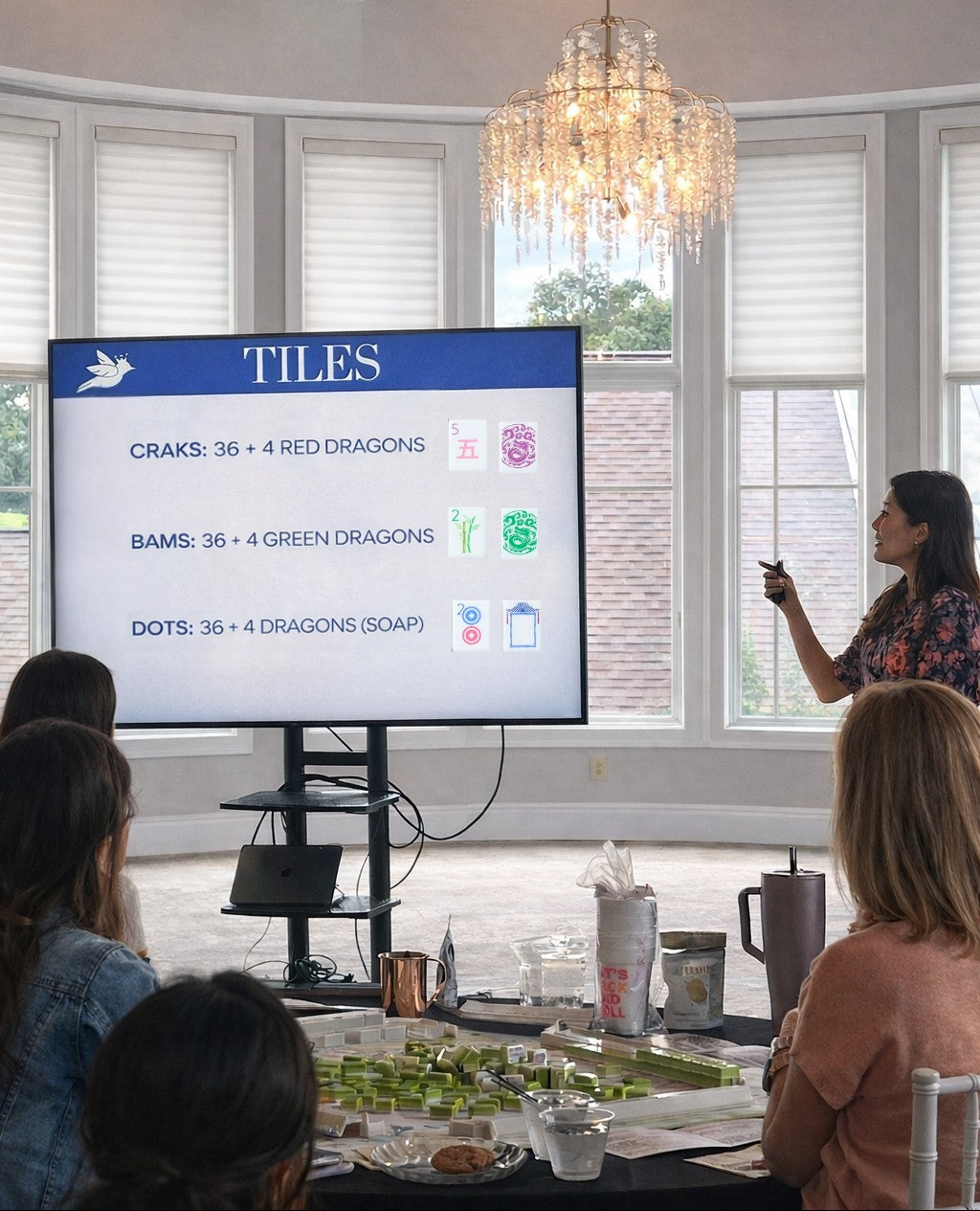 Woman giving a presentation in a modern room with large windows and a chandelier.
