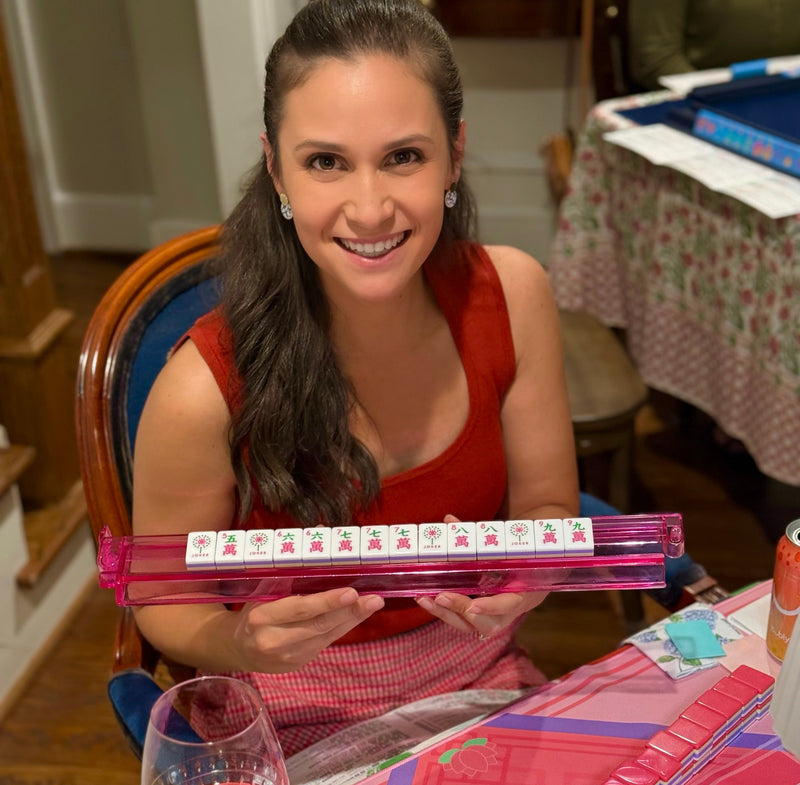 Woman holding a pink mahjong set with a glass of red wine on a table.
