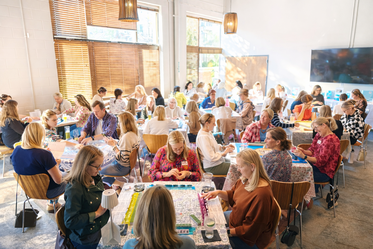 Group of people playing board games in a large room with windows.