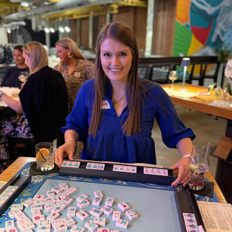 Woman playing mahjong in a casual indoor setting with other people and decor.