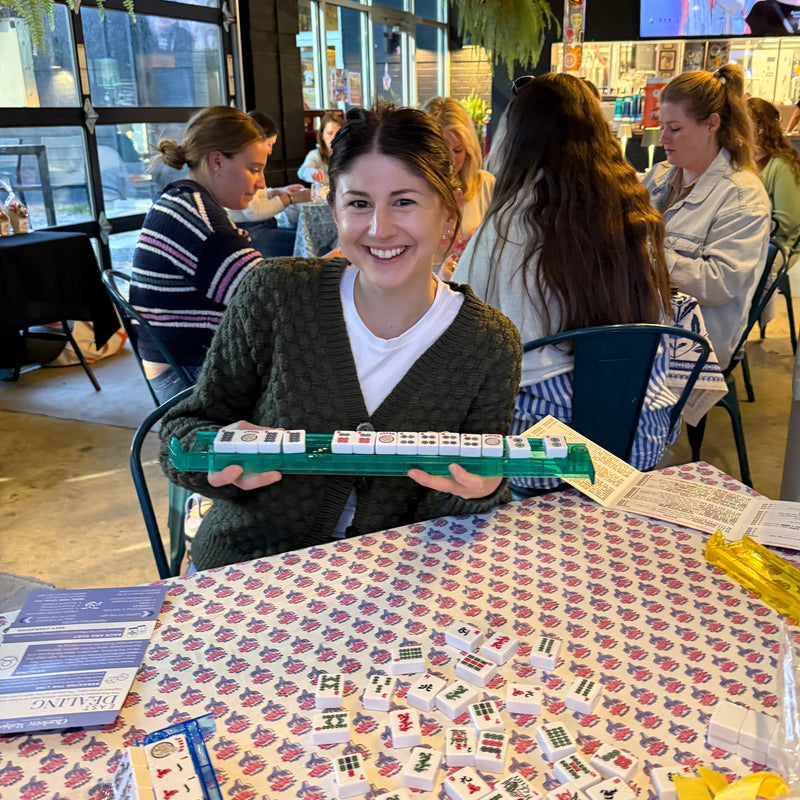 Woman holding a box of dominoes at a table with a domino game set up.